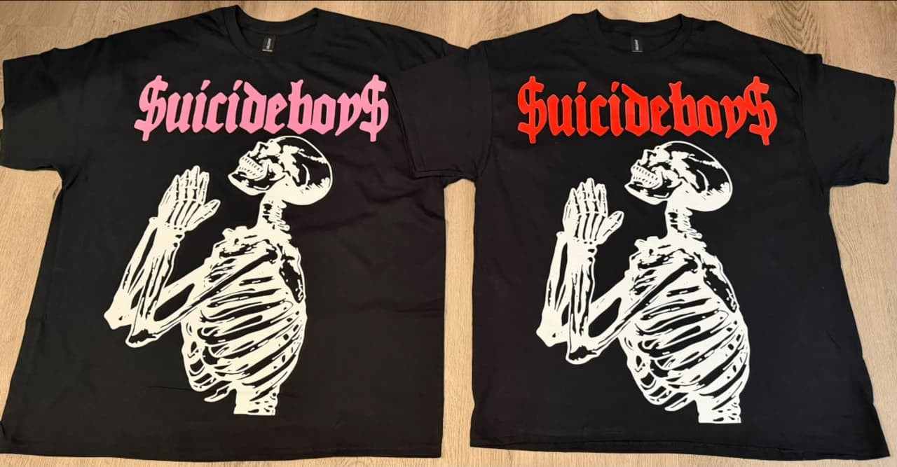 Two black Suicide Boyz concert tees with a praying skeleton graphic — pink lettering on the left, red on the right